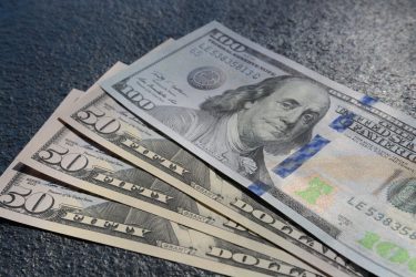 A closeup shot of three fifty and one hundred dollars bills on a gray background